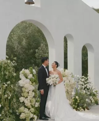 Bride and Groom smile at each other in front of modern altar surrounded by lush organic florals