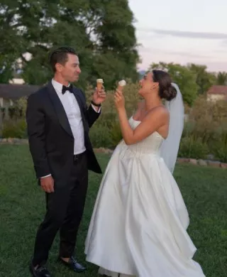 Bride and groom eat from ice cream cones on the ground of their outdoor wedding