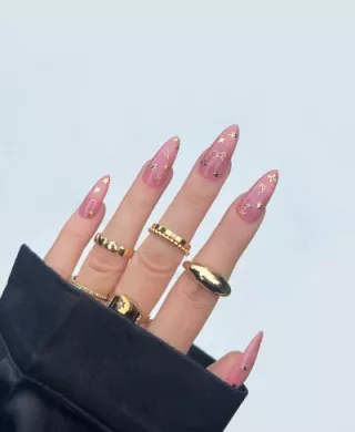 Hand peeking out of sweatshirt sleeve, with Deco Beauty nail sticker manicure and gold rings on fingers