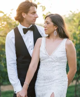 Bride and groom pose in their after party outfits with sunlit greenery in the background