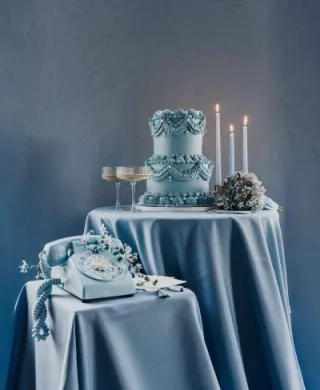 Dusty blue styled scene featuring After The Tone phone, two-tiered lambeth cake, candles and two glasses of champagne on silky tablecloths