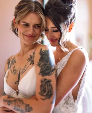 Couple holds each other in their arms, both wearing gorgeous wedding dresses during their first look