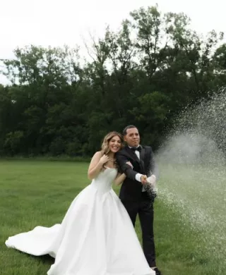 Bride and groom stand on lush grounds of Belle Âme Vineyard, sparying champagne to celebrate their wedding day