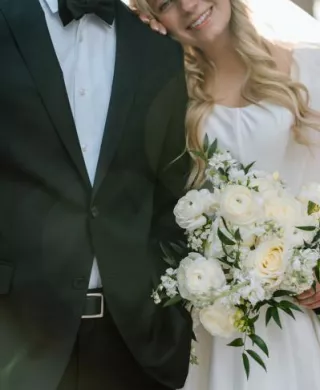 Bride rests her head on groom's shoulder, bouquet in hand on their wedding day at a family farm