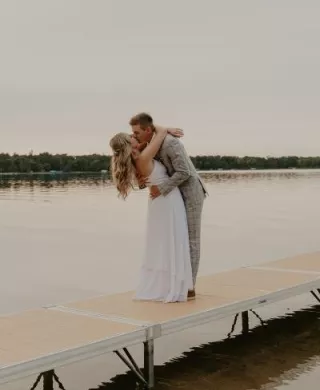Bride and groom share kiss on a dock with lake in background in lakeside wedding day