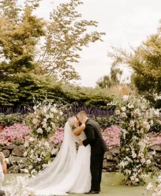 Kristin and Mason Share a Kiss in Front of Neutral Floral Arch After Exchanging Vows at Langdon Farms Golf Club