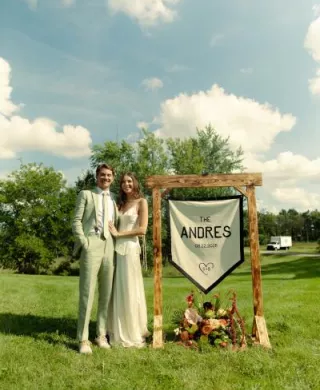 Sara and Billy stand by their custom made "Camp Andres" sign on their wedding day 