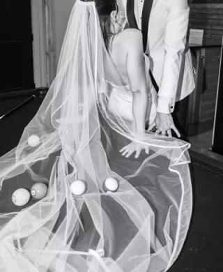 Bride and groom lean against the pool table with pool balls scattered throughout the bride's veil, in black and white