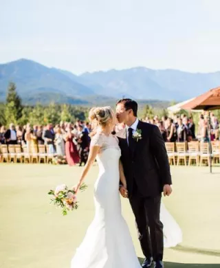 Bride and groom share a kiss after walking down the aisle in outdoor ceremony with mountainous backdrop at Tumble Creek