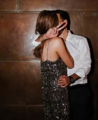 Bride and groom share a kiss in their festive after party clothes in front of a wooden wall at JM Cellars