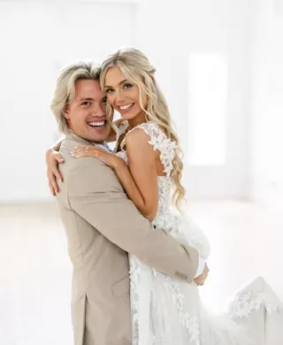 Groom embraces bride, lifting her up as they pose and smile on their wedding day at Redeemed Farm