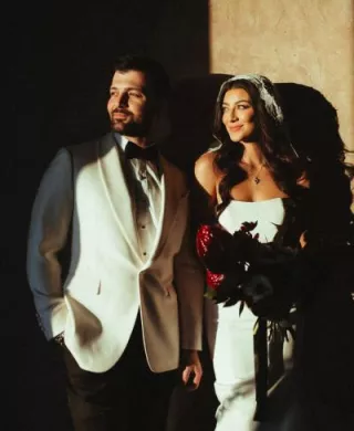Bride and groom pose against a wall with dramatic shadows cast over them