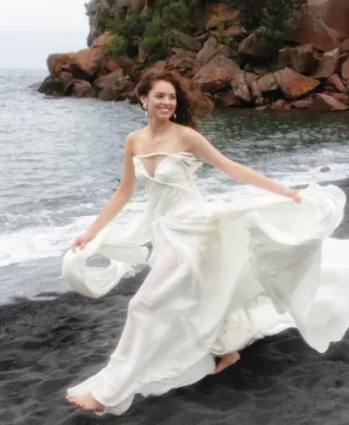 Model poses in fashion-forward wedding gown on the Black Sand Beach with Lake Superior in the background