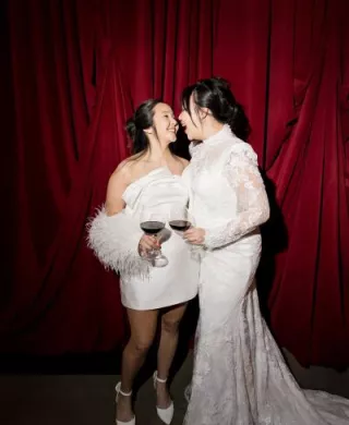 Models pose and share a kiss with drinks in hand in front of rich red draping