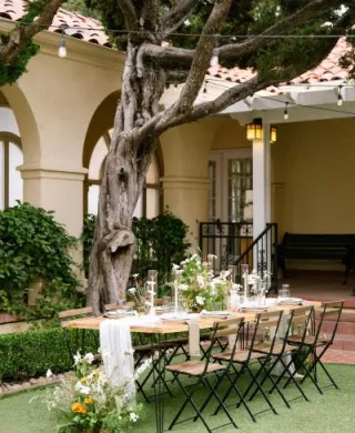 Table and chairs with nature-inspired decor and florals, underneath a large tree