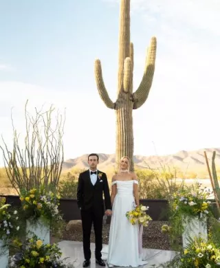 Bride and groom stand hand in hand at the altar, framed by bright blooms and cacti at The Willow Weddings & Event Center