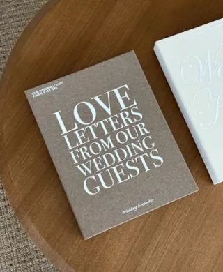 Brown linen keepsake box by The Ceremony Club with "Love Letters from our Wedding Guests" on cover, laying on wooden table