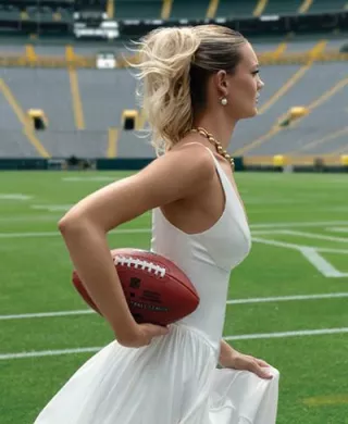 Model in bridal wear and jewelry poses running with football on Lambeau Field
