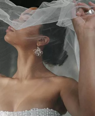 Model poses with holding veil over her face, showcasing stunning accessories in editorial shoot