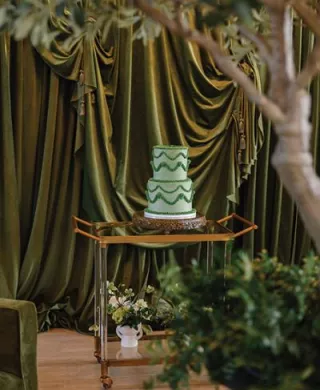 Green lambeth-style cake framed by greenery against a backdrop of dramatic green velvet draping at Westlin Hall