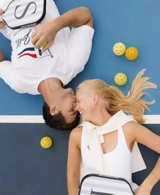 Jennifer and Sean lay on the pickleball court facing each other surrounded by pickleballs