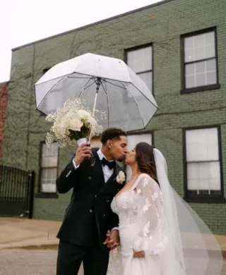 Bride and groom share a kiss under a clear umbrella outside of The Ivy House