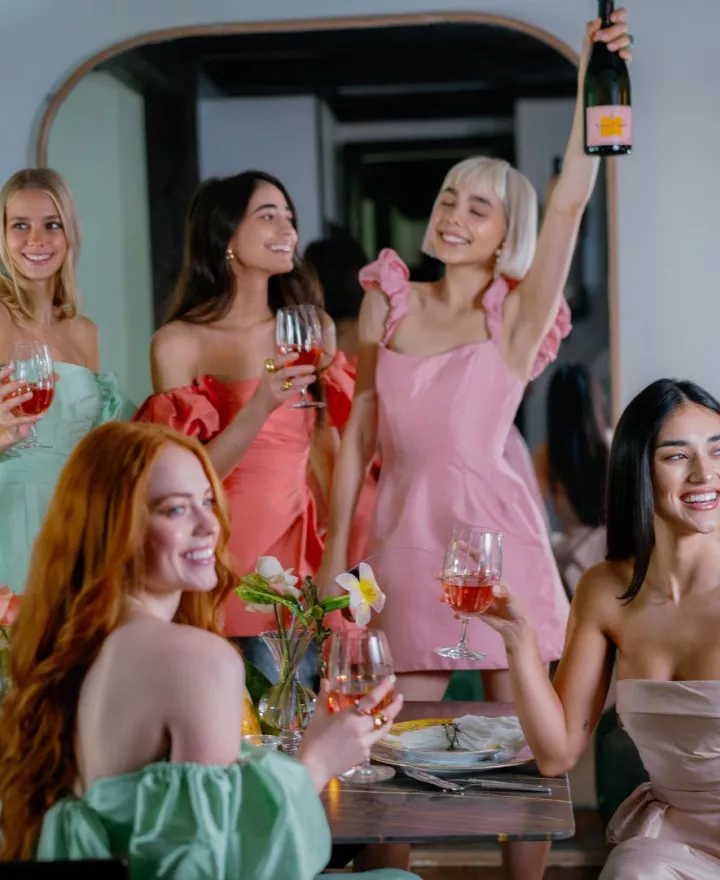 Models in bright-toned, summer-style occasionwear dresses from Watters toasting with Champagne.