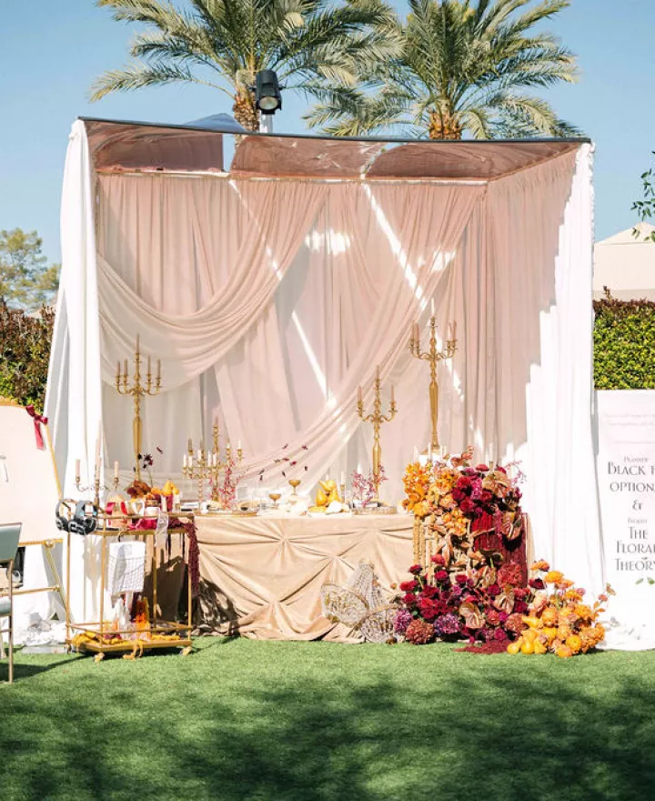 Elegant wedding table setup with draped fabric, gold candelabras, lush floral arrangements, and an interactive station featuring headphones and a writing station with ribbons.