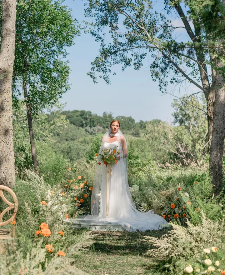 Model stands at the modern altar space, surrounded by lush organic florals in ceremony scene at Petal and Thorn Flower Farm