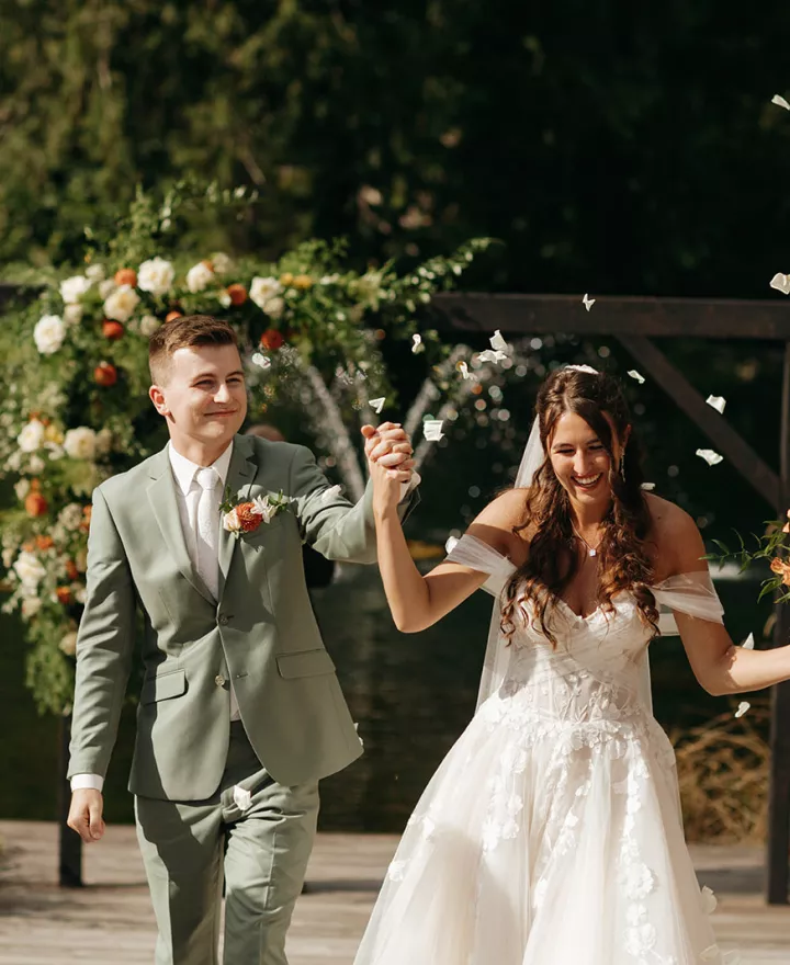 Bride and Groom hold hands and smile while walking back down the aisle