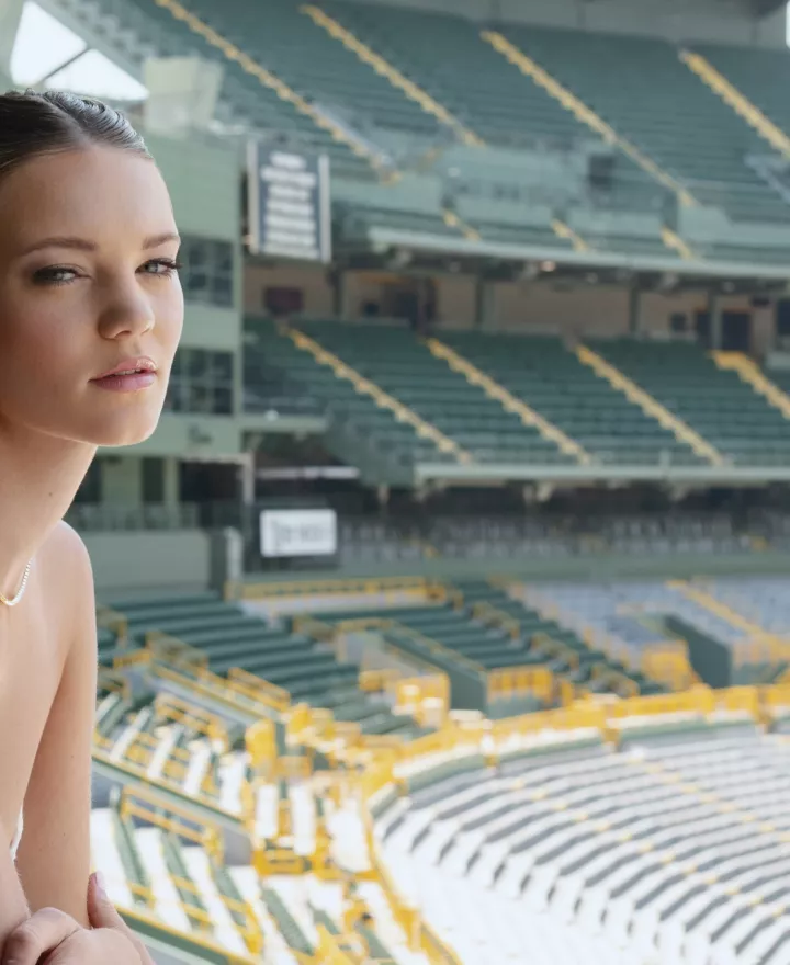 Model poses in bridal attire and jewelry looking over Lambeau Field