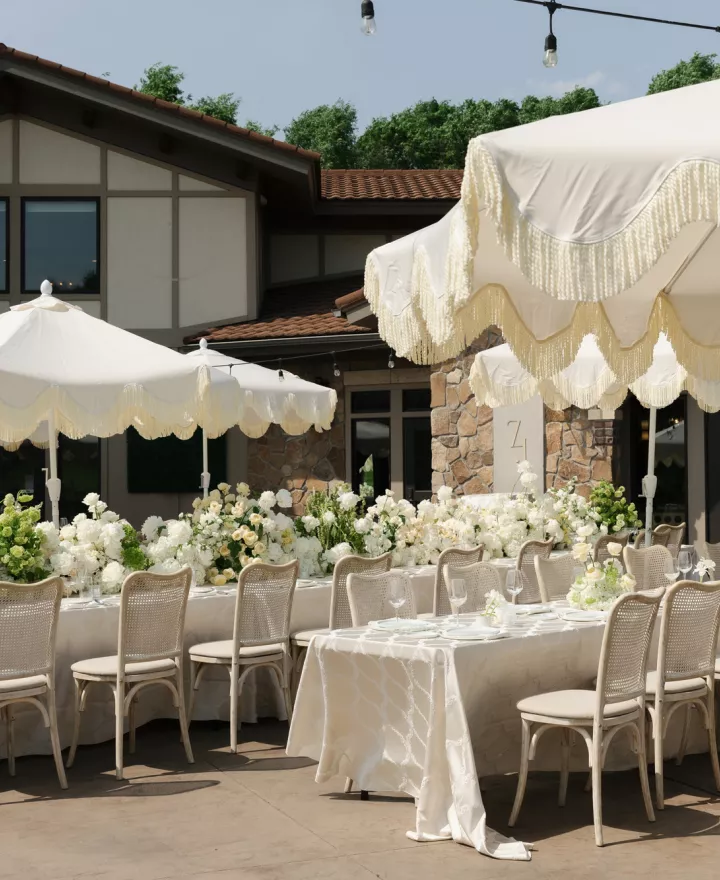 Long tablescapes shaded by soft yellow umbrellas, accented by lush florals in outdoor reception scene at Belle Âme Vineyard