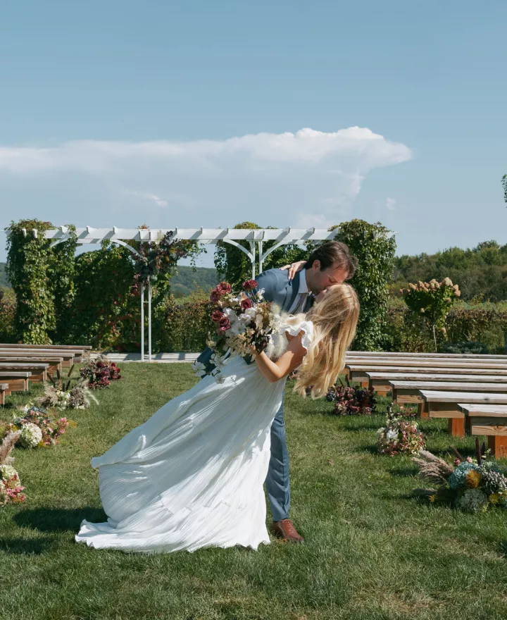 Groom dips bride and they share a kiss at the end of the aisle on the grounds of Rustic Roots Winery