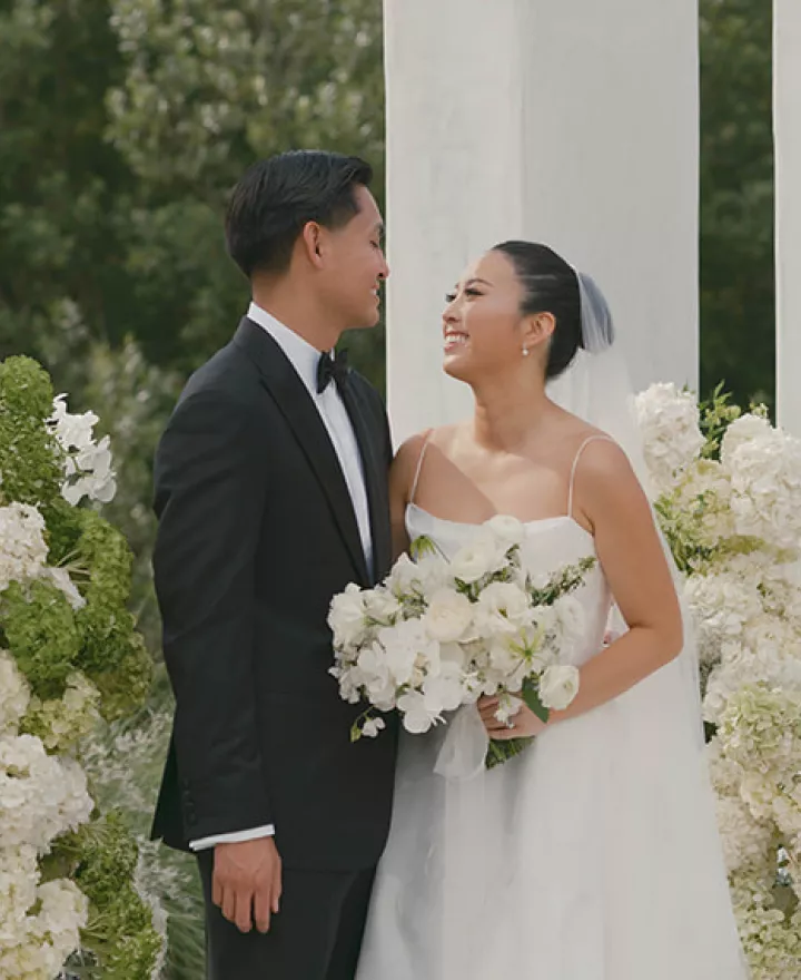 Bride and Groom smile at each other in front of modern altar surrounded by lush organic florals