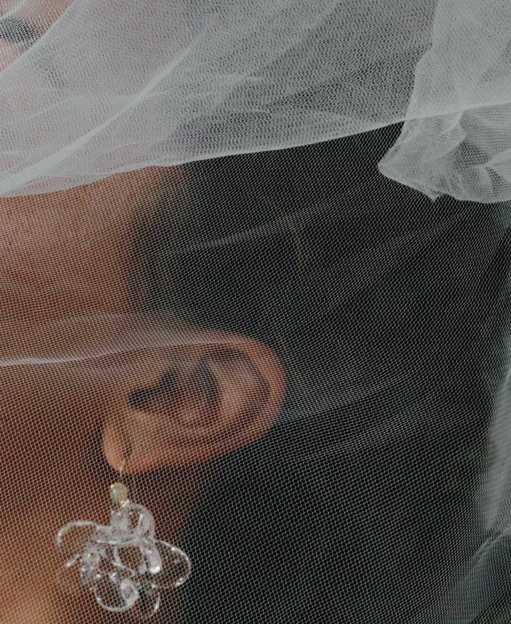Model poses with holding veil over her face, showcasing stunning accessories in editorial shoot