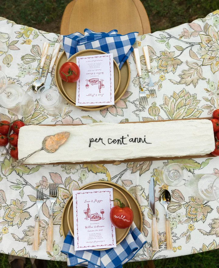 Horizontal cake with "per cent'anni" written in frosting on Italian-inspired tablescape featuring tomatoes as décor