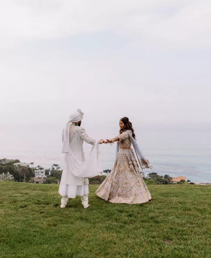 Bride and groom stand hand in hand with the misty coastline in the background