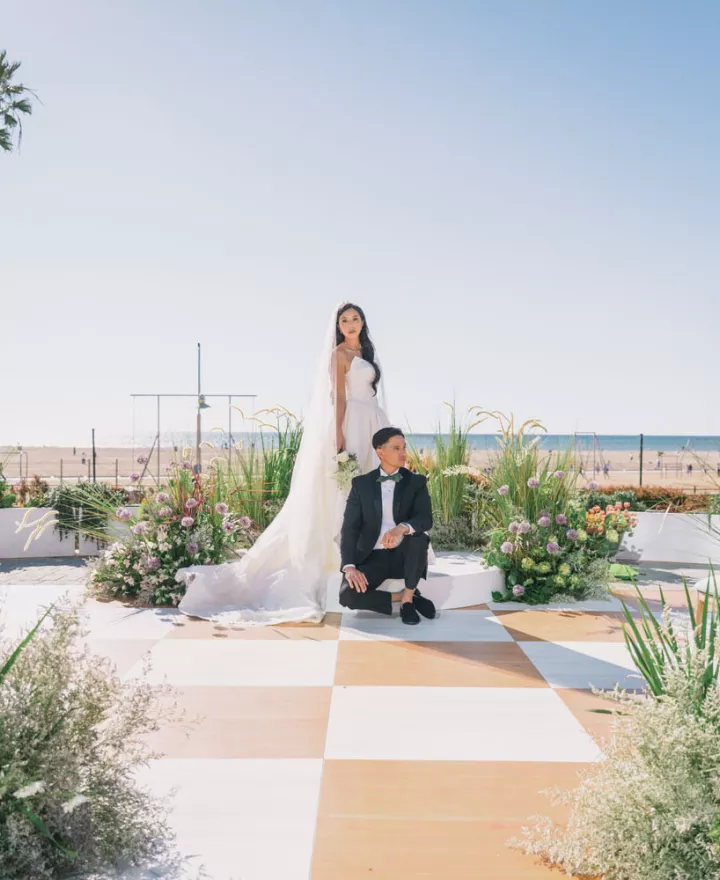 Bride and groom pose at a modern beachfront wedding ceremony setup at Regent Santa Monica with ocean views, palm trees and colorful floral arrangements