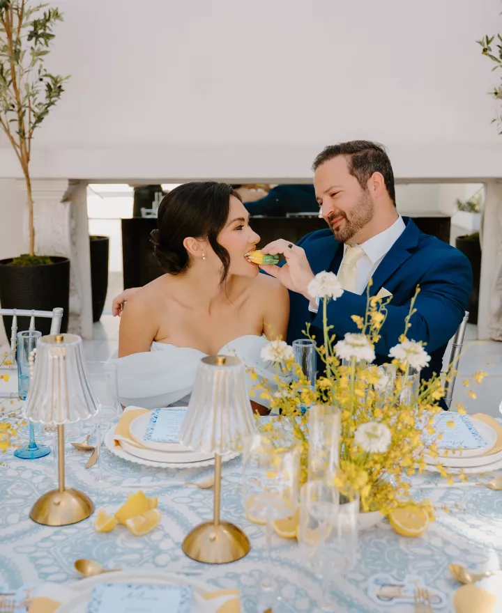 Groom feeds bride a lemon shaped macaron at an Amalfi Coast inspired tablescape 