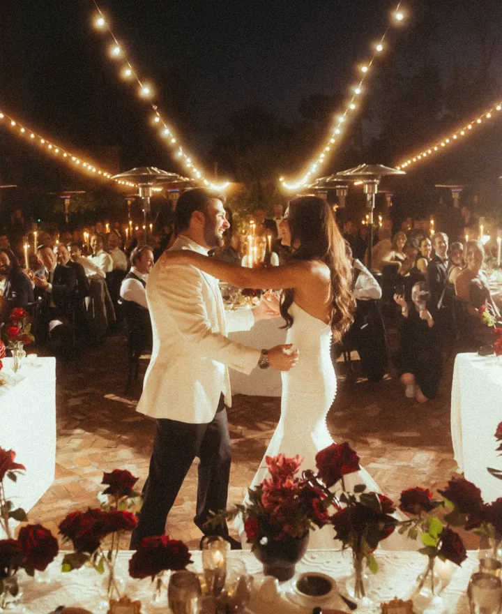Bride and groom share a dance framed by their candlelit outdoor reception featuring bold red flowers at Royal Palms Resort and Spa