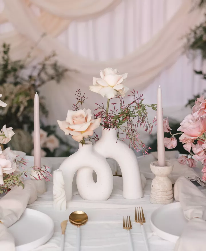 Tablescape featuring rosy hues and sculptural stone vases in imagined reception