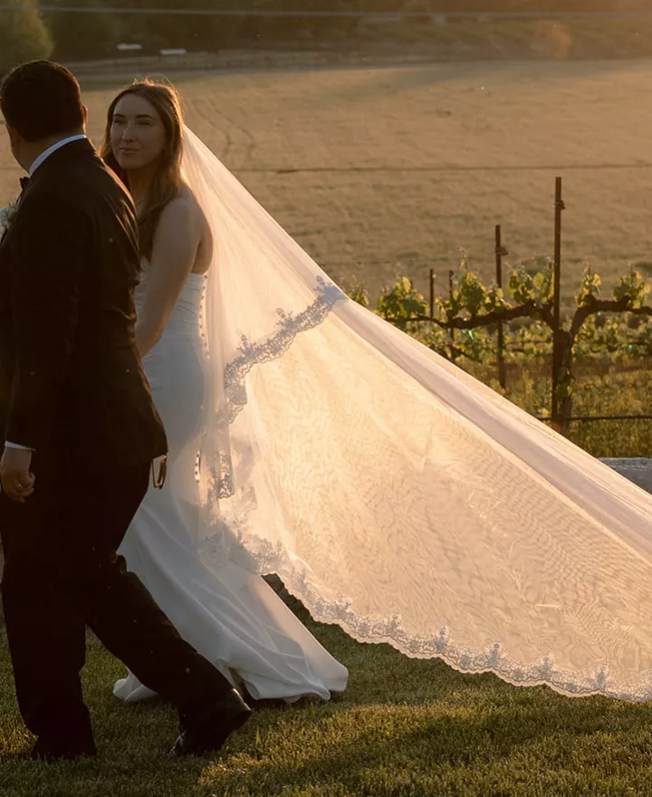 Bride and groom walk hand in hand on the grounds of Hearst Ranch Winery during golden hour