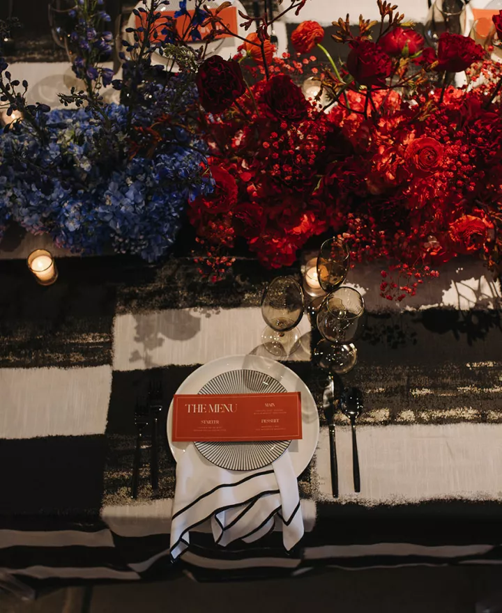 Maximalist tablescape featuring black and white checkered tablecloth and ombre rainbow florals