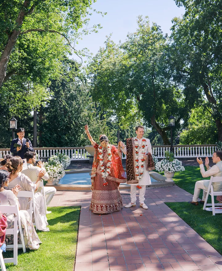 Bride and groom raise their hands in celebration while walking back down the aisle in outdoor ceremony at Lairmont Manor