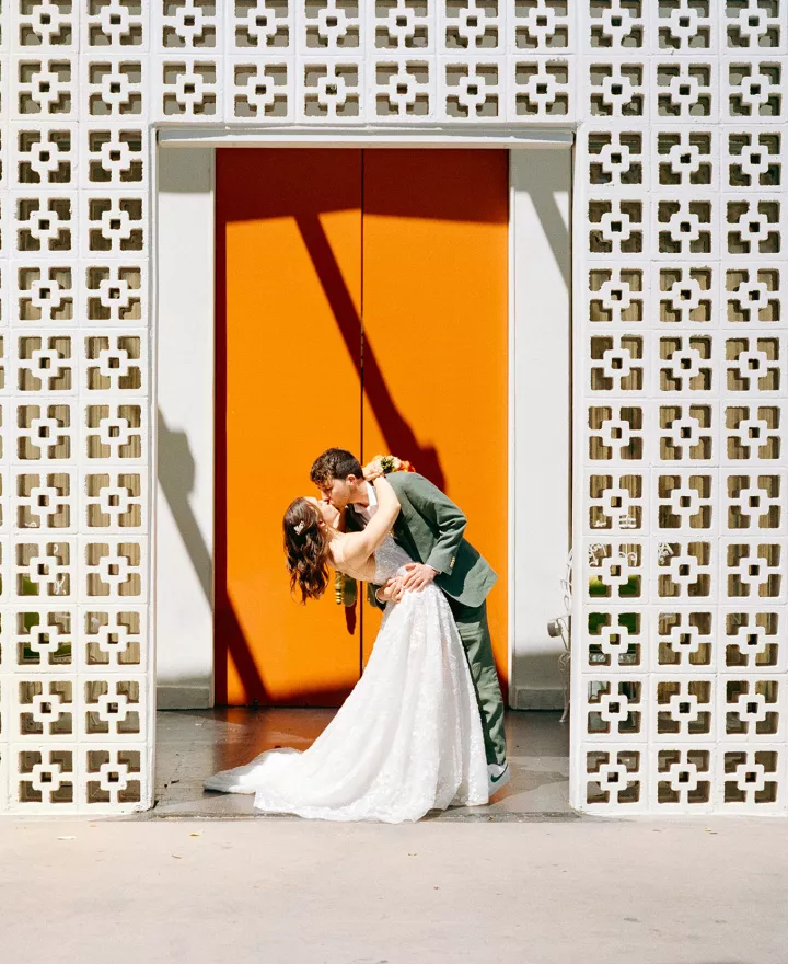 Bride and groom share a kiss against orange door in wedding day at Parker Palm Springs 