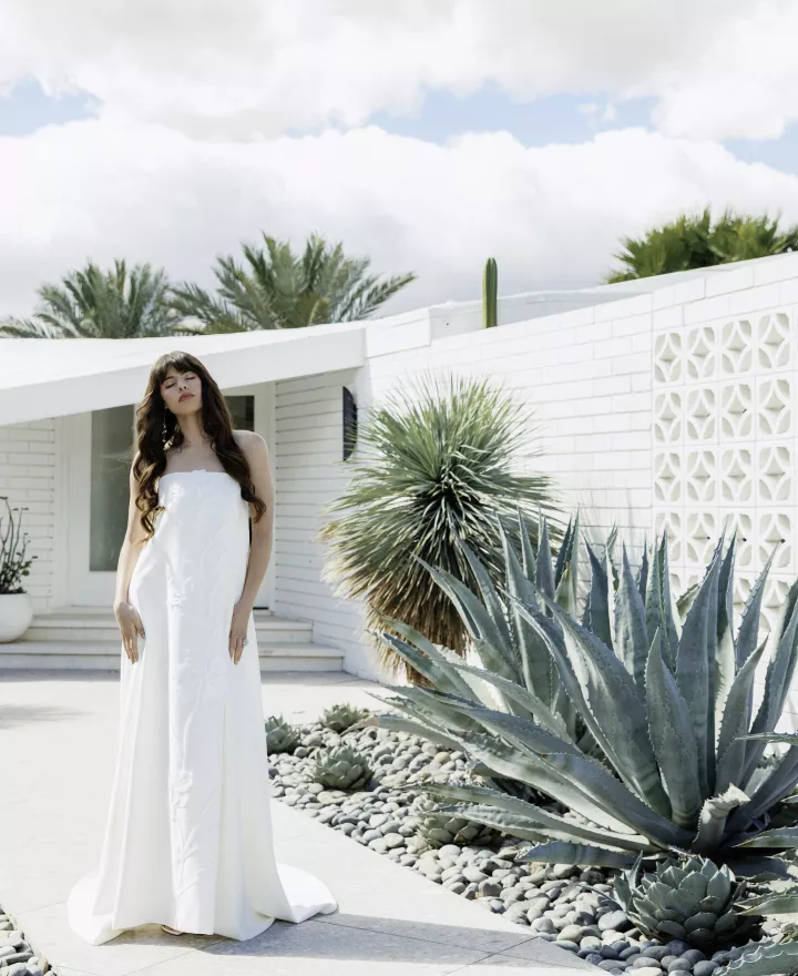 Model poses in front of Desert White House in strapless wedding dress with subtle floral details