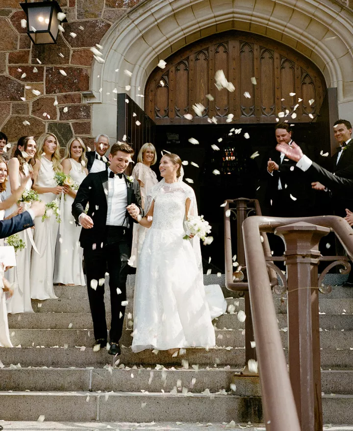 Isabel and John descend the staircase after ceremony t Plymouth Congregational Church as petals waft through the air
