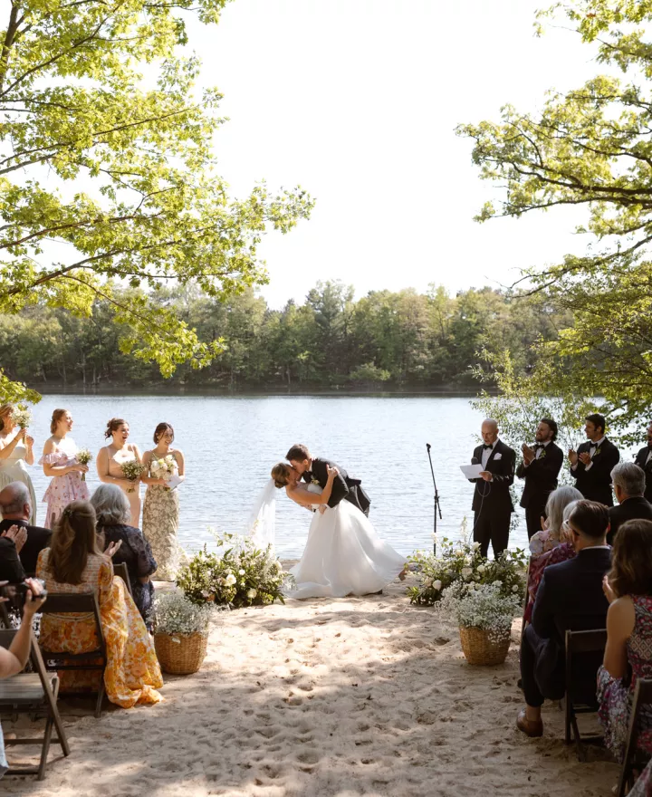 Molly and Ralph kiss at the altar in their outdoor ceremony framed by trees and their loved ones at Camp Elsewhere