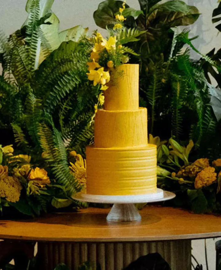 Bold, mango-hued tiered cake surrounded by lush verdure in imagined wedding day 