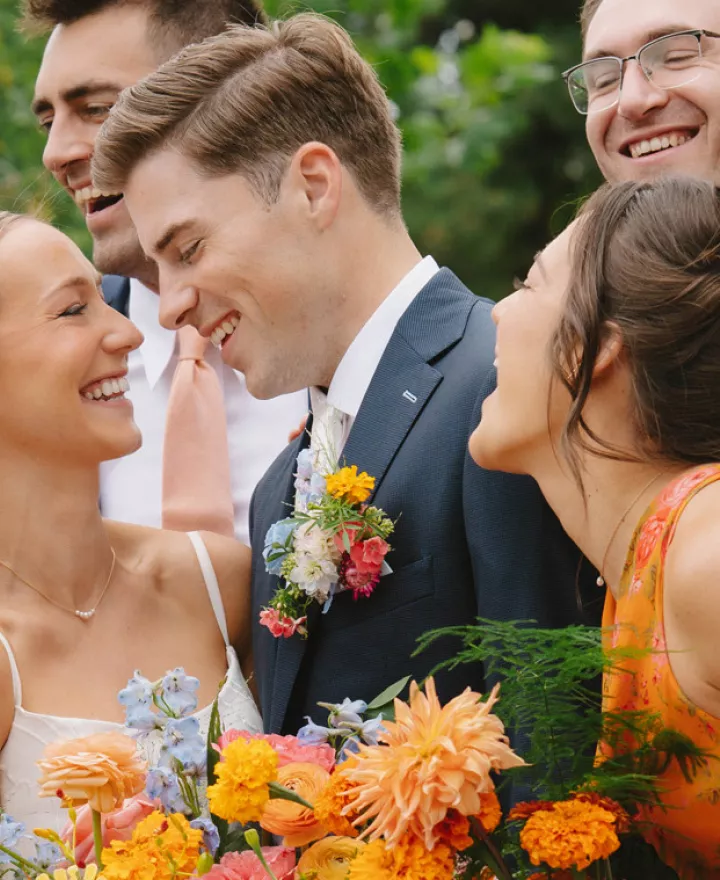 Wedding party surrounds the bride and groom as they share a loving glance